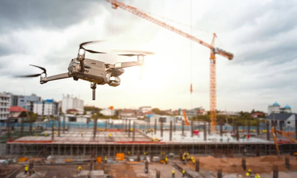 Drone surveying a busy construction site with workers and cranes in the background, illustrating modern land surveying technology in construction.
