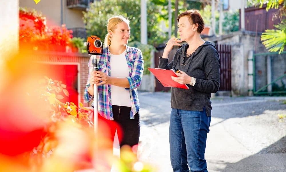 Two people reviewing property details next to surveying equipment during a due diligence survey before closing