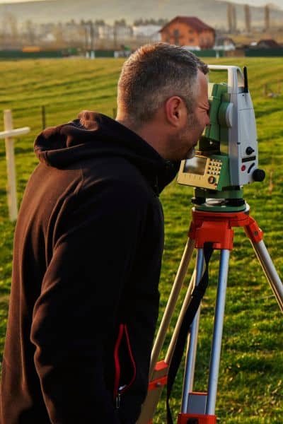 Surveyor checking yard - ALTA SURVEY Miami Surveyor checking property line markers in a yard using professional equipment