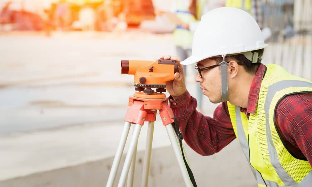 Surveyor using theodolite on construction site - ALTA SURVEY Miami A licensed surveyor examining land measurements with a theodolite at an active construction site