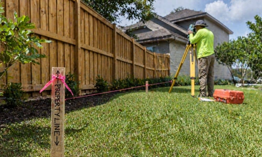 Survey stakes and measuring line showing a property boundary survey near a residential fence