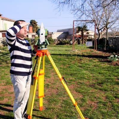 Land surveying total station field work - ALTA SURVEY Miami Surveyor using a total station in an open field during a land survey showing how measurements are taken in boundary survey cost calculations